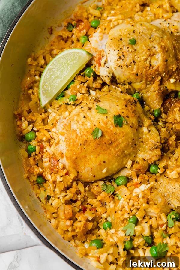 A vibrant pan of low-carb cauliflower arroz con pollo, garnished with fresh cilantro and lime wedges, ready to be served.