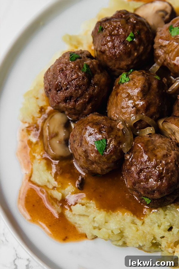 A close-up of Salisbury Steak Meatballs, perfectly coated in a rich brown gravy, garnished with fresh herbs.