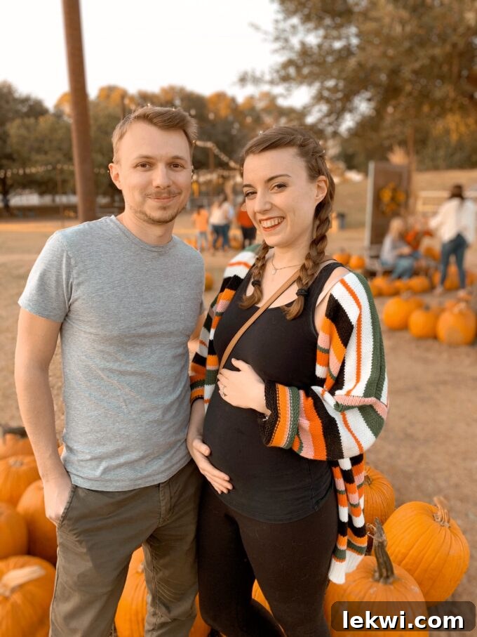 Michelle pregnant and holding her belly next to Daniel at a pumpkin patch.