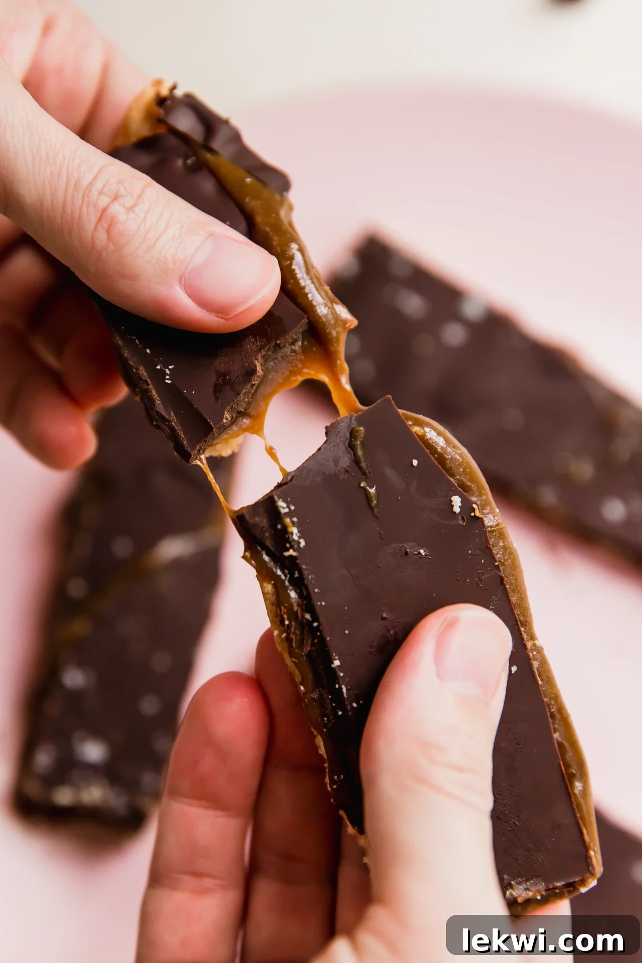 Homemade Twix bar being broken in half with golden caramel stretching deliciously.