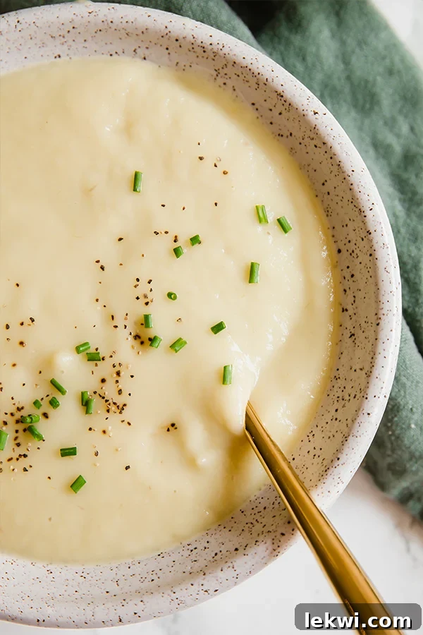 A white bowl filled with creamy sweet potato leek soup, garnished with fresh herbs.