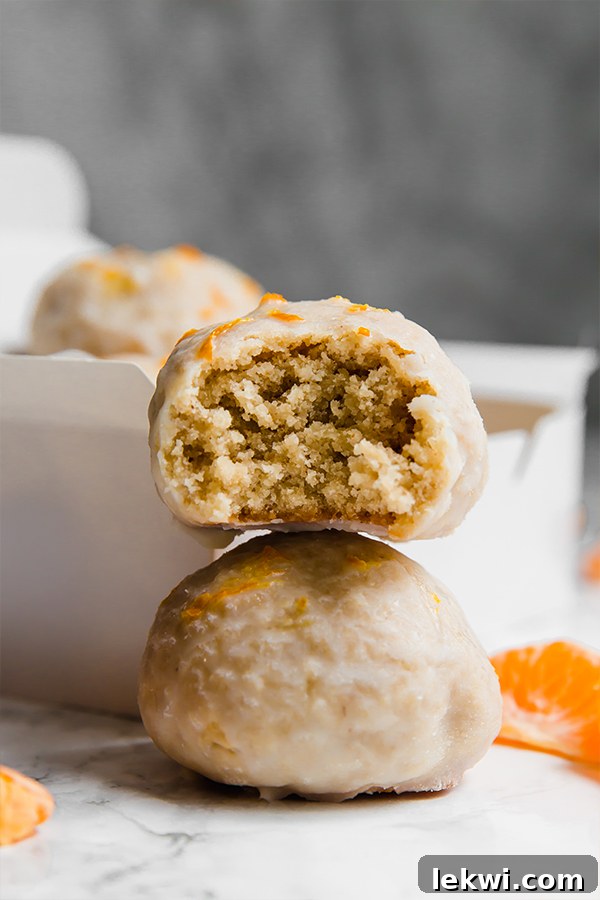 Two mandarin donut holes stacked on top of each other with a bite taken out of the top one.