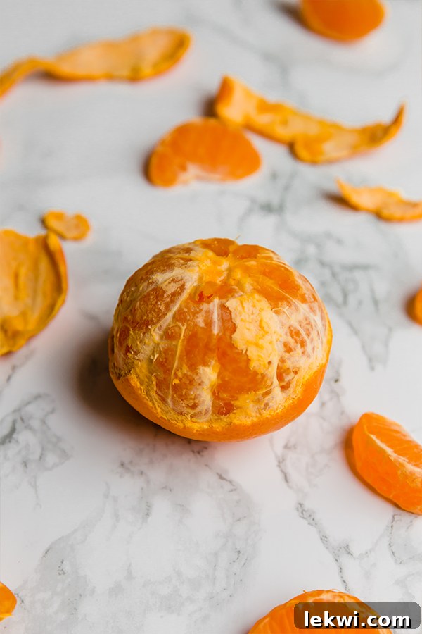 A mandarin that has been partially peeled sitting on a counter.