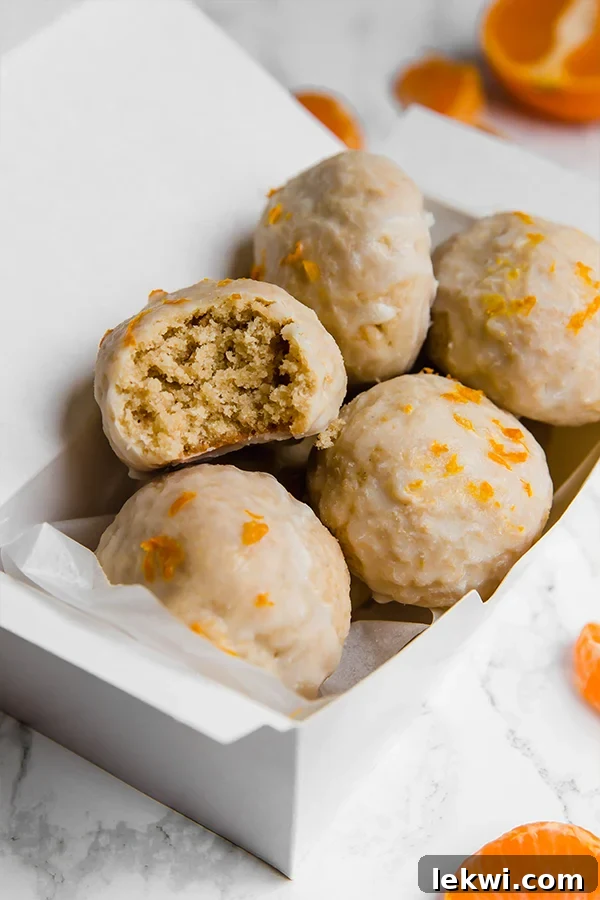 A white container filled with mandarin donut holes with a bite taken out of one of them.