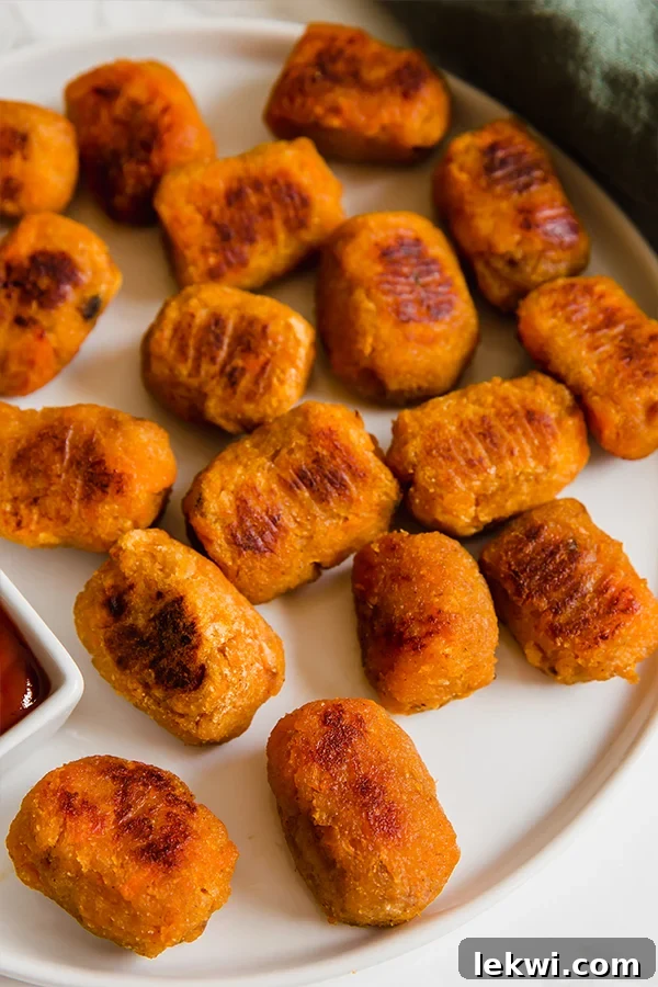 A white plate topped with butternut squash tots and a dipping sauce nearby.