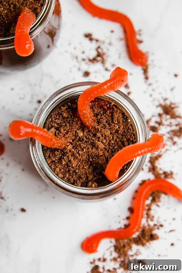 A glass jar of "dirt cup" topped with gummy worms.