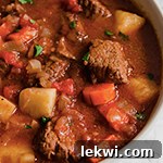 A white bowl filled with Greek Inspired Tomato Beef Stew.