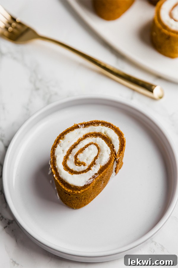 A beautifully sliced piece of Paleo AIP Pumpkin Roll, revealing its intricate pumpkin cake spiral and creamy frosting.