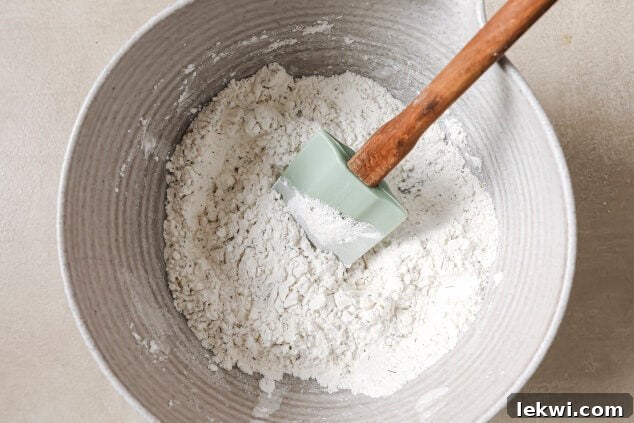 Dry ingredients in a bowl with a spatula, ready to be mixed for AIP dinner rolls.