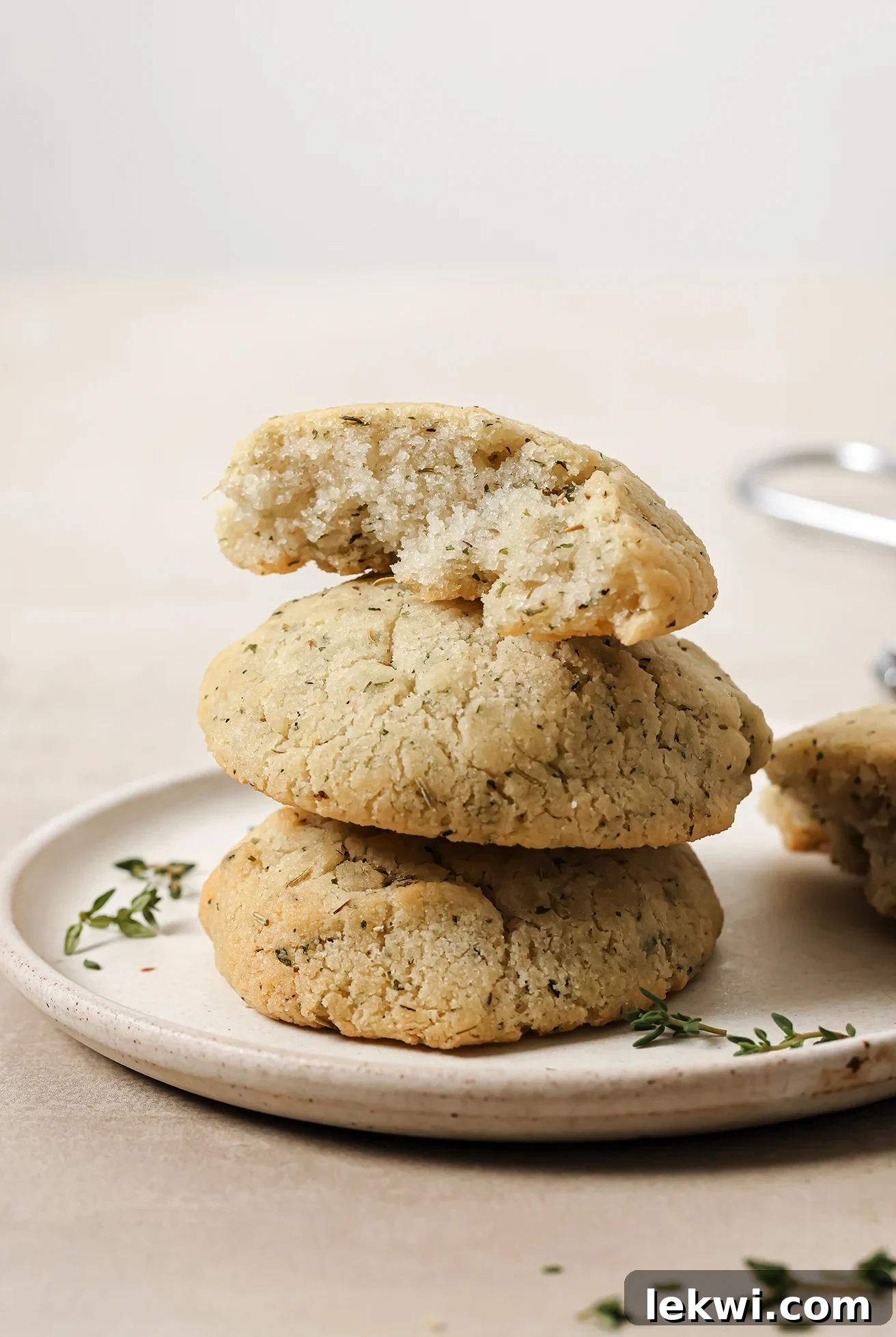 A stack of three warm garlic & herb dinner rolls on a white plate, garnished with fresh thyme on the side.