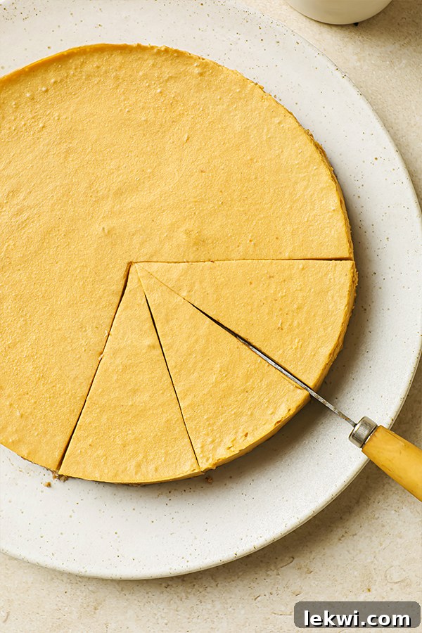 A chilled cheesecake on a plate, being expertly cut into neat slices with a knife.