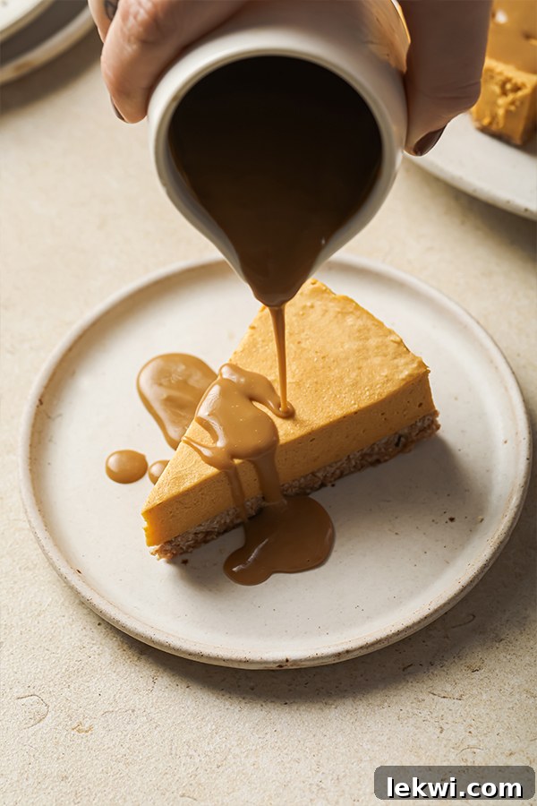 Smooth, rich caramel sauce gracefully pouring over a single slice of pumpkin cheesecake, ready to be enjoyed.