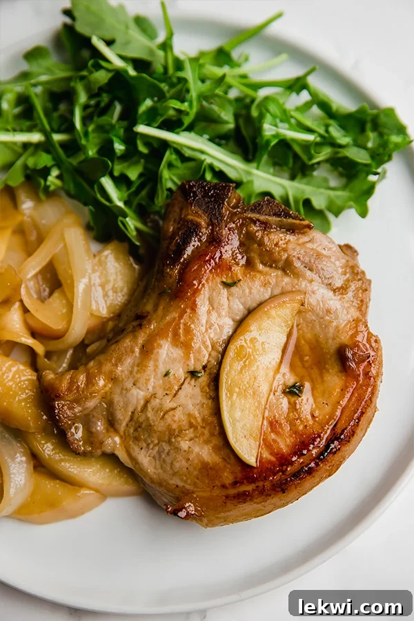 A beautifully seared apple pork chop on a white plate, accompanied by a fresh arugula salad, showcasing the golden-brown crust and vibrant apple slices.