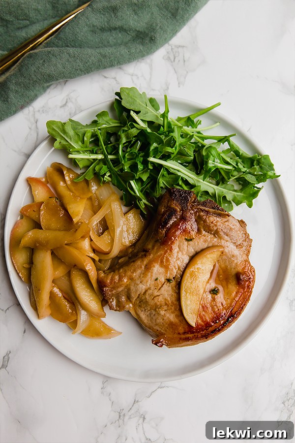 A close-up of a serving of apple pork chops on a white plate, highlighting the perfectly cooked pork, tender apple slices, and a vibrant green garnish.