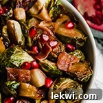 A white bowl with roasted brussels sprouts, apples, and bacon in it.