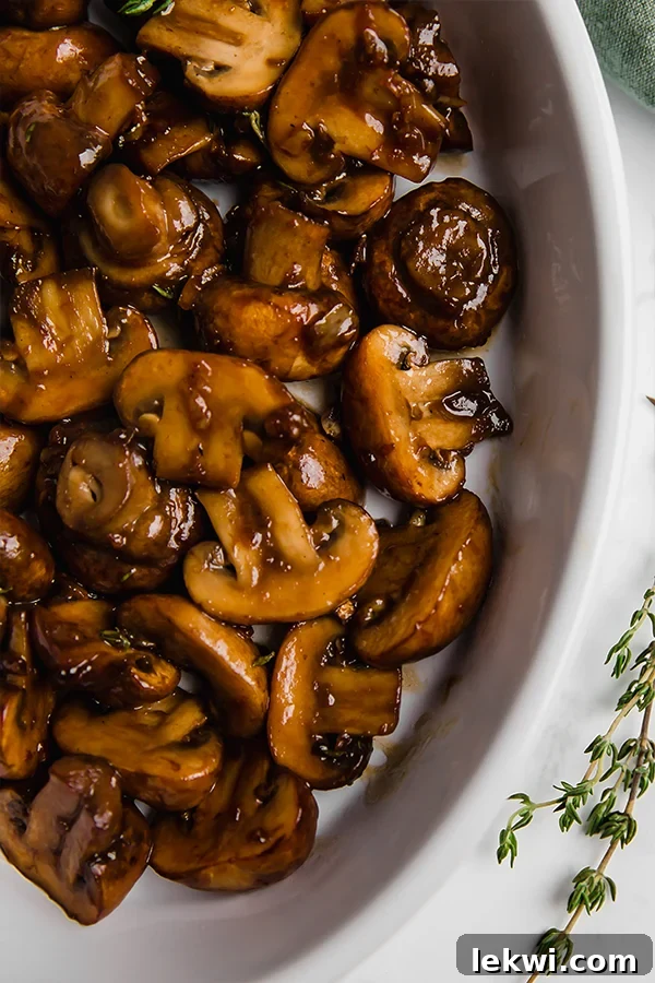 A beautifully presented white ceramic dish filled with glossy, dark garlic balsamic mushrooms, garnished with fresh herbs.