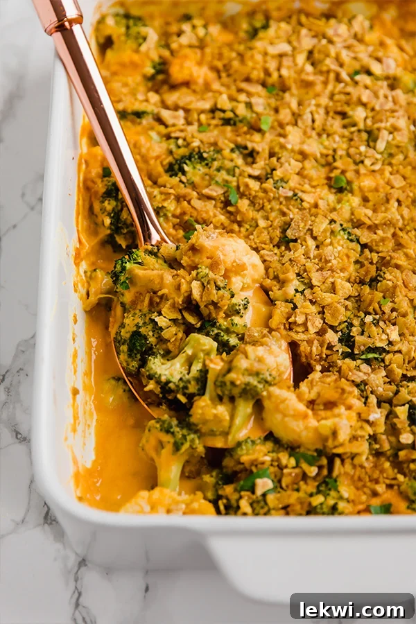 A white baking dish filled with healthy broccoli cheese casserole with a serving spoon ready to take a scoop out.