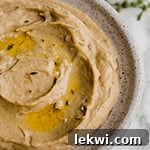 A white bowl filled with roasted cauliflower & parsnip mash topped with olive oil and fresh herbs.