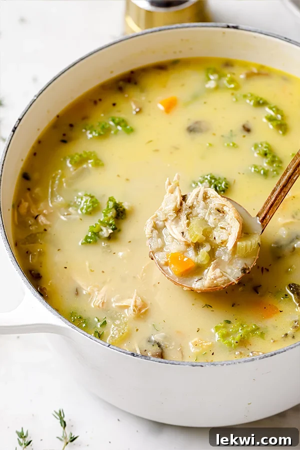A large white Dutch oven filled with a rich, creamy turkey and vegetable soup. A serving spoon is lifting a scoop of the soup, highlighting its comforting texture and visible vegetables.