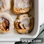 A white baking dish with aip cinnamon rolls fully baked with glaze over it.