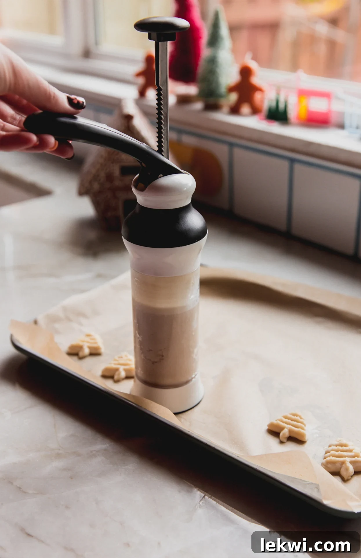 A cookie press pressing spritz cookies onto a lined baking sheet.