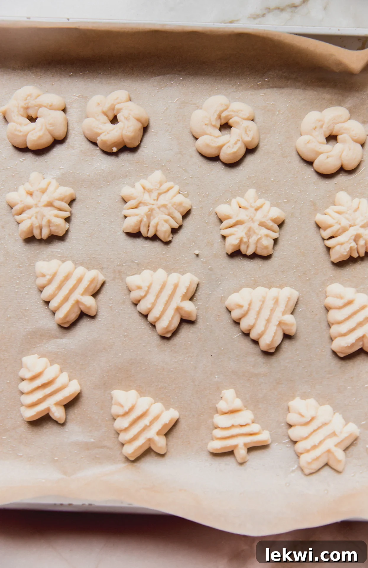 Spritz cookies in festive shapes, unbaked on a baking sheet.