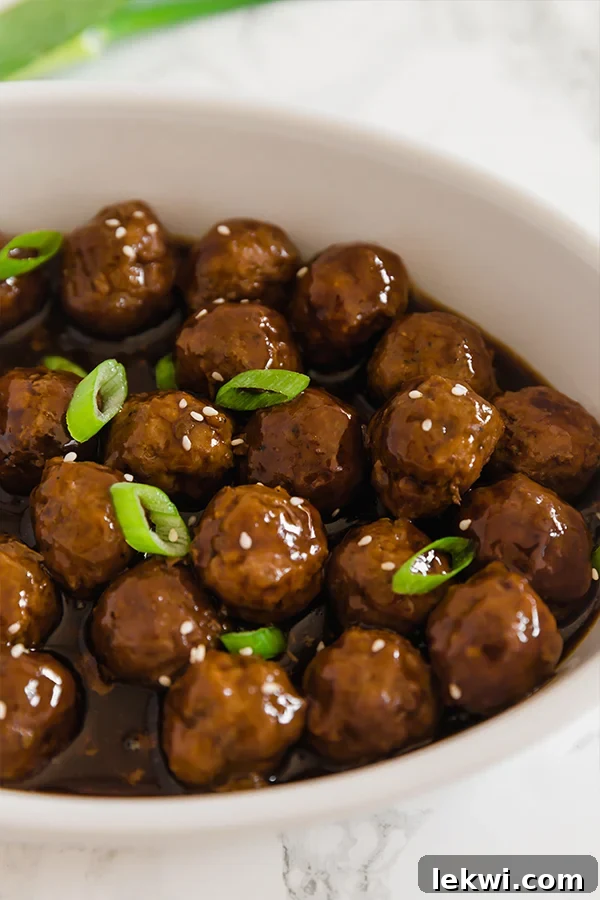 A white bowl filled with glistening Mongolian beef meatballs, generously topped with vibrant green onions, ready to be served as an appetizer or main dish.