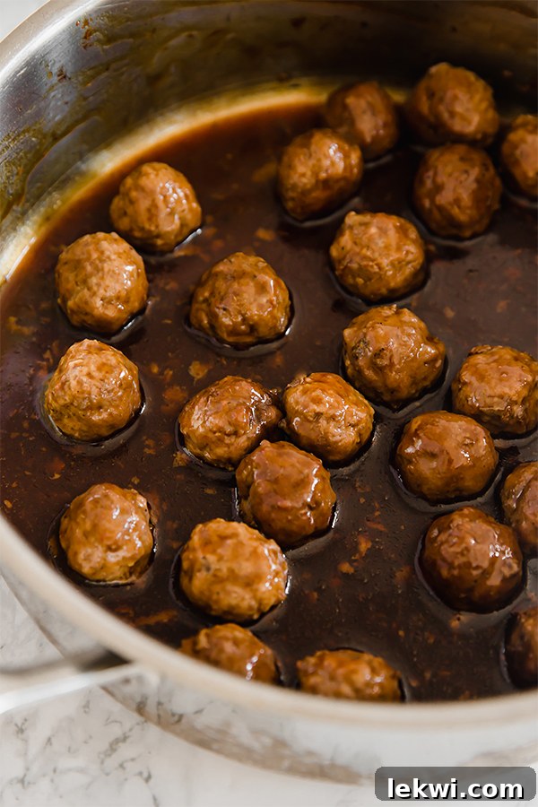 Close-up of Mongolian Beef Meatballs in a white bowl, glistening with sauce and topped with fresh green onions, showcasing their appetizing texture and readiness to eat.