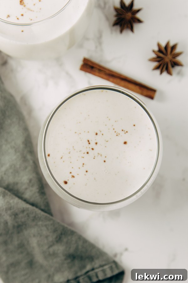 A clear glass filled with creamy, golden eggnog, accompanied by a warm cinnamon stick, ready to be enjoyed during the festive season.