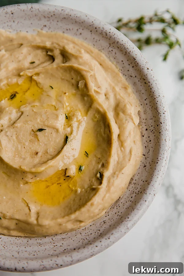 A rustic ceramic bowl brimming with a velvety smooth roasted cauliflower and parsnip mash, garnished with fresh herbs, ready to be served as a comforting side dish.