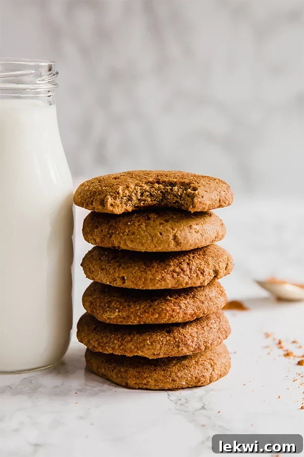 A stack of gingersnap cookies next to a glass container of nut milk with a bite taken out of the top cookie.