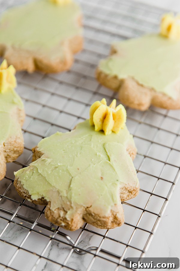 A wire rack with sugar cookies cut out into Christmas trees with green icing and yellow stars made out of icing.