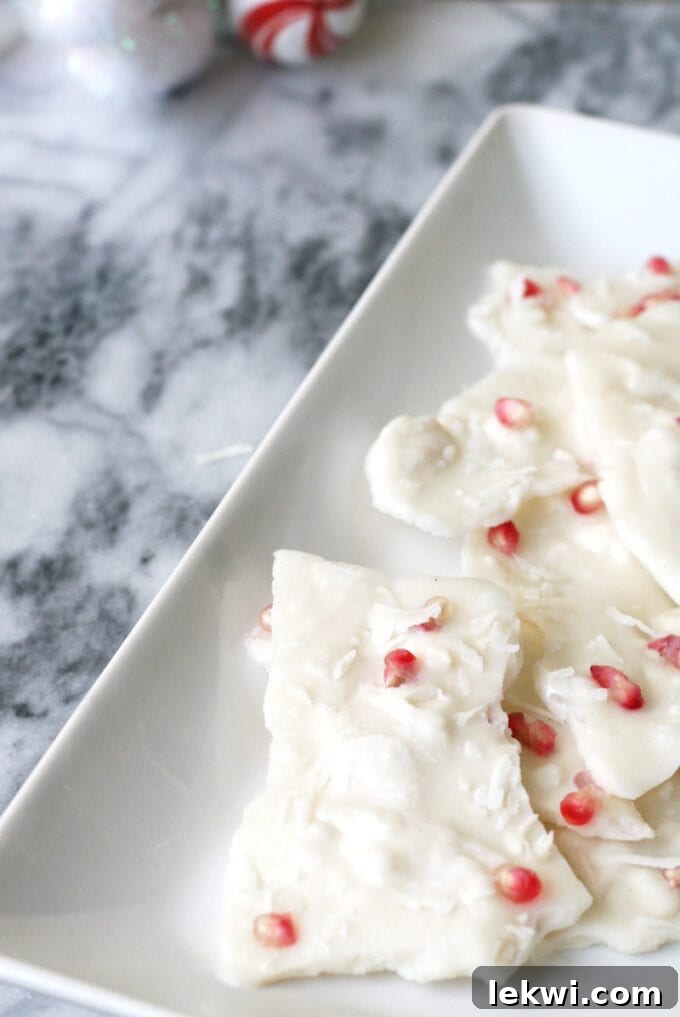 A white ceramic dish with peppermint bark topped with pomegranate seeds on it.