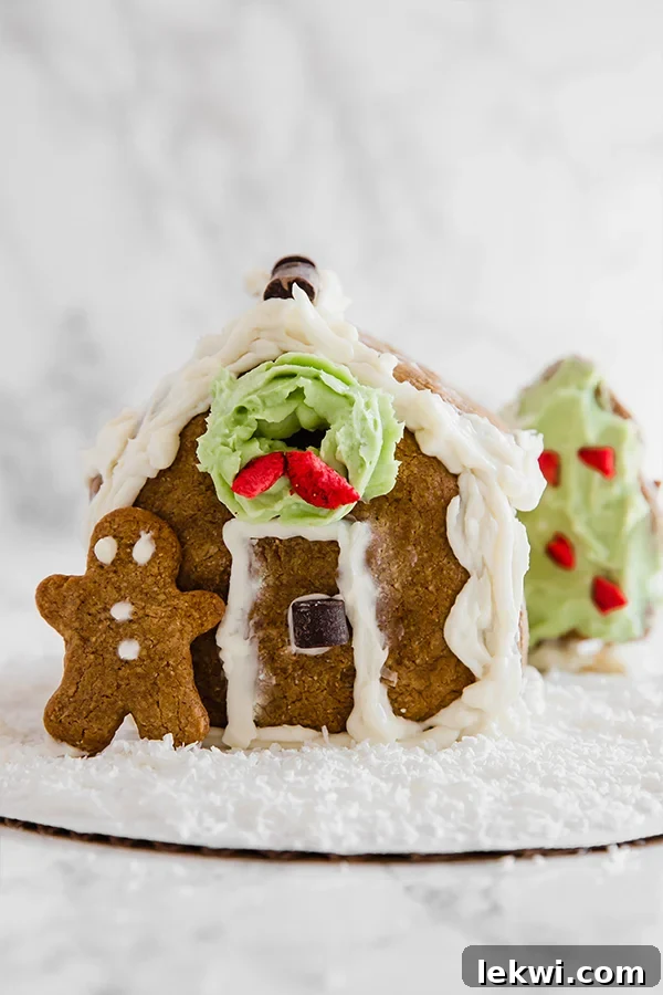 A homemade gingerbread house with a gingerbread man leaning against it. 