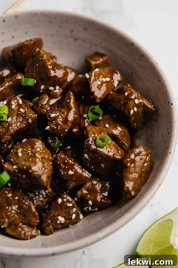 A beautifully plated bowl of glistening teriyaki steak bites, generously topped with vibrant green onions, ready to be enjoyed.
