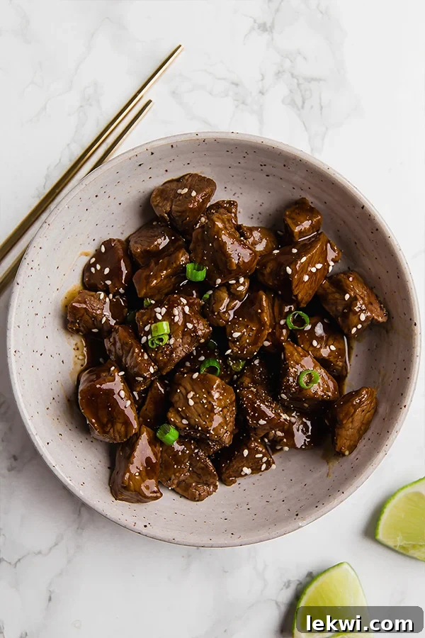 A vibrant bowl of teriyaki steak bites, expertly seared and coated in a glossy sauce, garnished with fresh green onions.