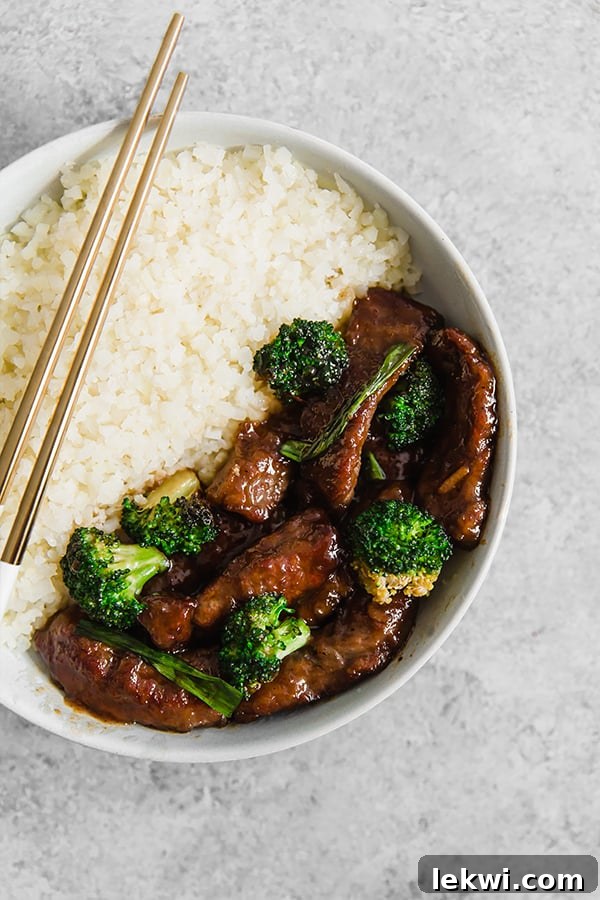 A white bowl with cauliflower rice and mongolian beef stir fry.
