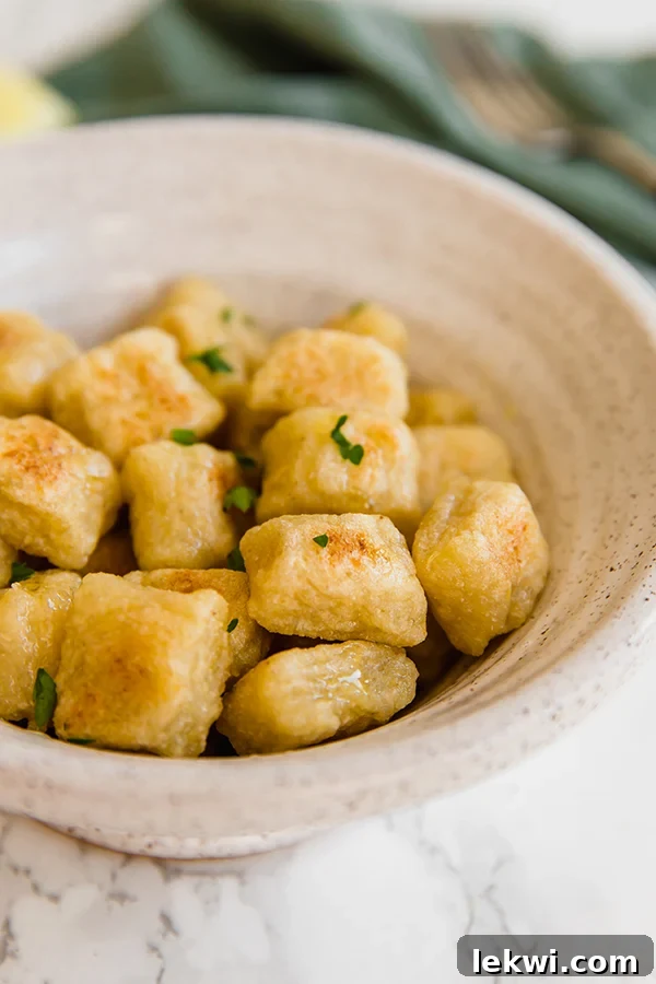 A white ceramic bowl filled with cauliflower gnocchi topped with fresh herbs.