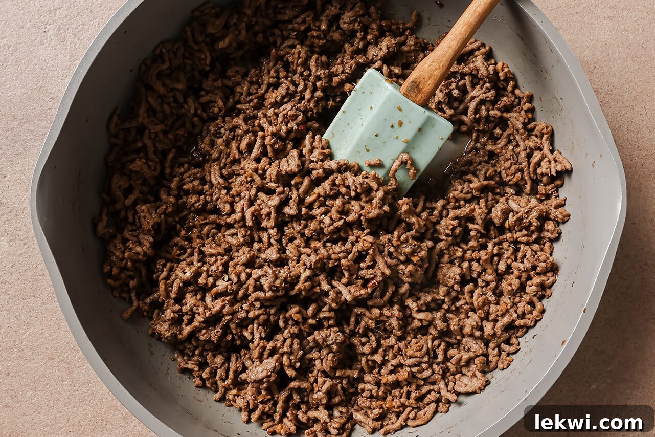 Cooked ground beef in a large skillet, coated in a glistening sauce. The beef appears fully browned and the sauce is bubbling slightly, indicating it's reducing and infusing flavor into the meat.
