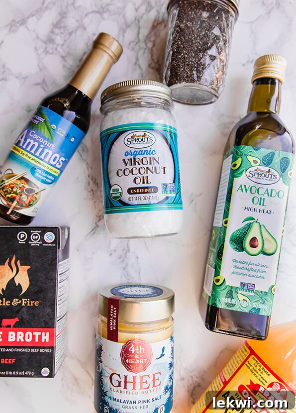 Avocado oil, coconut oil, coconut aminos, bone broth, and ghee lying on a counter.