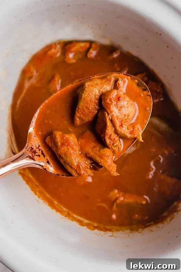 A slow cooker filled with Indian butter chicken, with a serving spoon scooping out a portion.