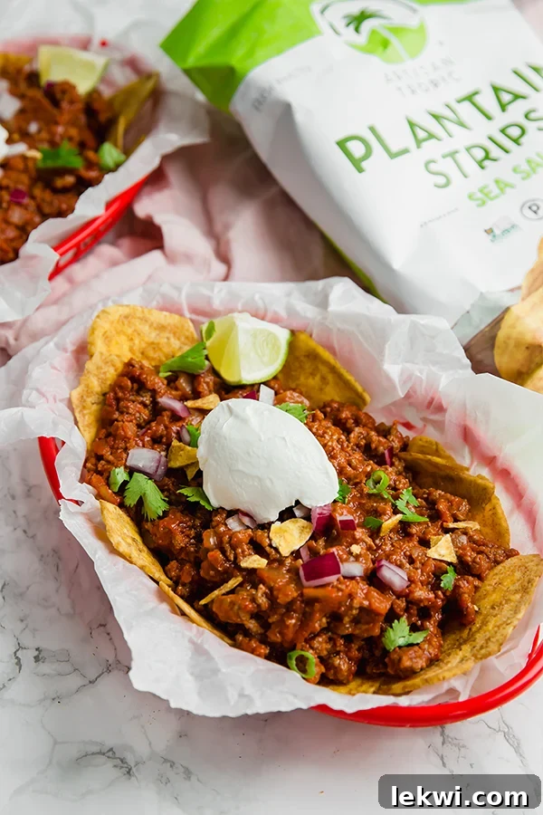 A red basket filled with frito pie over plantain chips with fresh lime wedges.