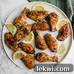 A white plate filled with lemon pepper chicken wings and slices of lemon.