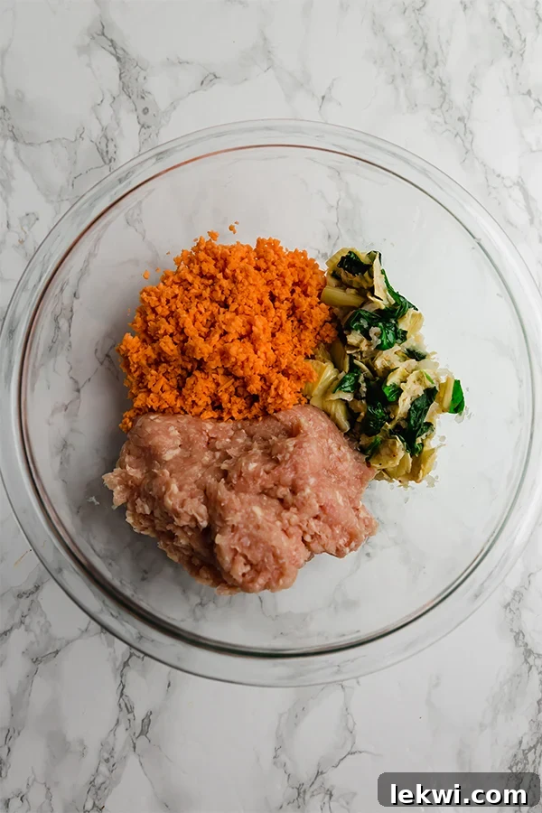 A glass bowl containing the raw mixture for spinach and artichoke sweet potato chicken poppers, showcasing the vibrant ingredients before shaping and baking.