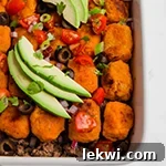 A white baking dish filled with sweet potato tater tot taco casserole topped with avocado slices.