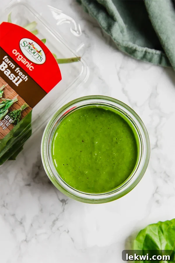 A glass jar filled with pesto sauce next to a container of fresh basil.