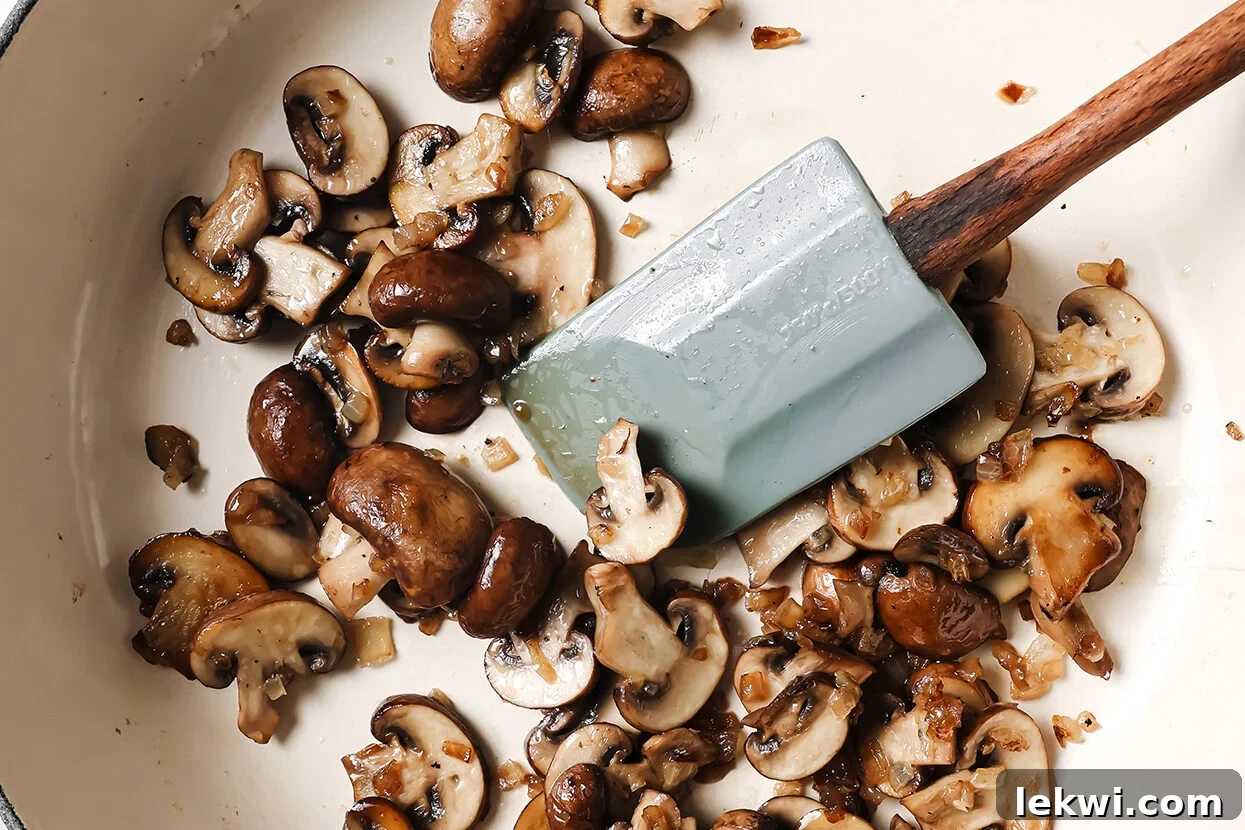 Sliced mushrooms being cooked in a pan with a spatula, starting the Florentine sauce base.