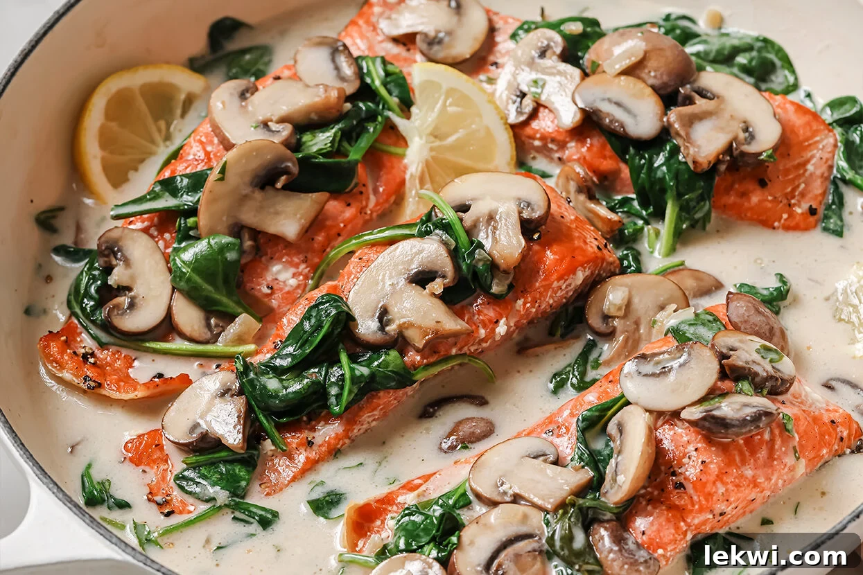 Cooked salmon florentine in a pan topped with mushrooms, spinach, and lemon wedges, ready to serve.