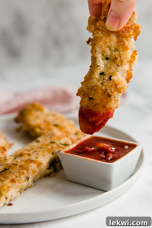 A white plate topped with homemade chicken tenders with one being dipped into a small container of dipping sauce.