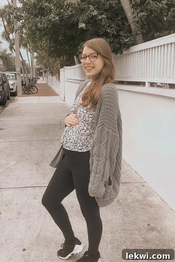 Michelle pregnant standing on a sidewalk smiling at the camera and holding her belly.